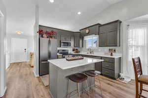 Kitchen featuring appliances with stainless steel finishes, light wood-type flooring, gray cabinetry, a kitchen island, and lofted ceiling