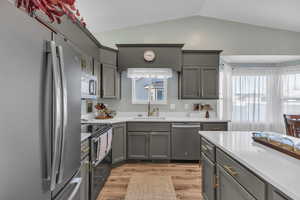 Kitchen with appliances with stainless steel finishes, vaulted ceiling, sink, light hardwood / wood-style flooring, and gray cabinets