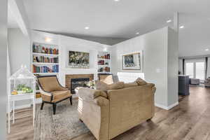 Living room featuring radiator heating unit, a brick fireplace, built in features, light hardwood / wood-style flooring, and lofted ceiling