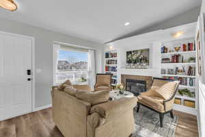 Living room featuring a tiled fireplace, built in features, vaulted ceiling, and light hardwood / wood-style flooring