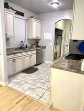 Kitchen with dark stone counters, sink, light hardwood / wood-style flooring, dishwasher, and white cabinetry