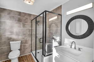 Bathroom with an enclosed shower, vanity, hardwood / wood-style flooring, tile walls, and toilet