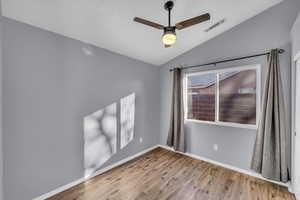 Spare room with hardwood / wood-style floors, plenty of natural light, ceiling fan, and vaulted ceiling