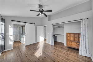 Unfurnished bedroom with ceiling fan, wood-type flooring, a barn door, connected bathroom, and a closet