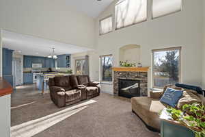 Family room with carpet, a towering ceiling, and stone hearth around gas fireplace. Shows dining area and kitchen.