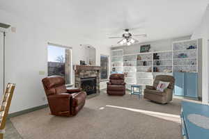 Living room featuring carpet, a stone fireplace, and ceiling fan.