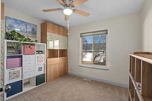 Bedroom used as office with light colored carpet and ceiling fan. Cabinets and desk built into closet are included. Cubby shelves are not.