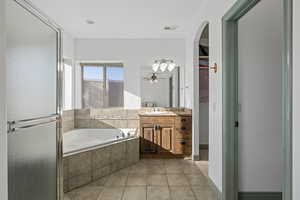 Ensuite bathroom with tile floors, soaker tub, separate toilet room, plus walk in shower, vanity, and ceiling fan