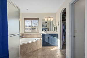 Primary ensuite bathroom featuring tile floors, ceiling fan, separate shower and tub, and vanity. Toilet is in a seperated area with a door.