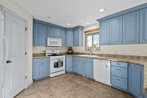 Kitchen with blue cabinetry, white appliances, light granite-tile counters, pantry, and sink