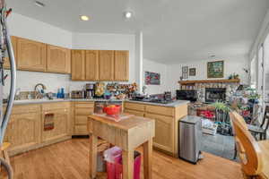 Kitchen with sink, light brown cabinets, gas cooktop, light hardwood / wood-style floors, and a fireplace