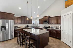 Kitchen with stainless steel appliances, light stone counters, decorative light fixtures, decorative backsplash, and a kitchen island
