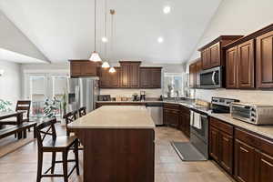 Kitchen with a center island, hanging light fixtures, decorative backsplash, appliances with stainless steel finishes, and light stone counters