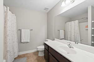 Bathroom featuring vanity, curtained shower, toilet, and a textured ceiling