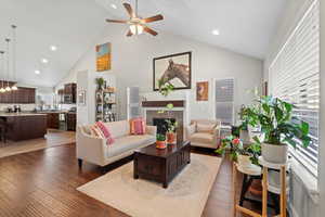 Living room with dark hardwood / wood-style floors, ceiling fan, high vaulted ceiling, and a tiled fireplace