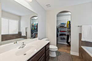 Bathroom featuring tile patterned flooring, a relaxing tiled tub, toilet, and vanity