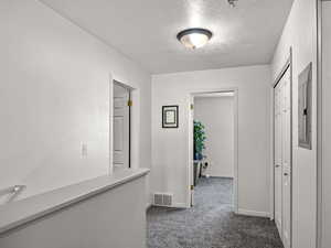 Hallway featuring a textured ceiling and dark colored carpet