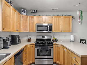 Kitchen featuring a breakfast bar, sink, light brown cabinetry, kitchen peninsula, and stainless steel appliances