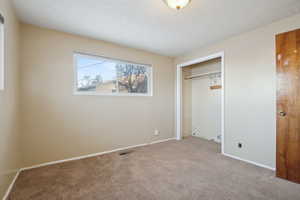 Unfurnished bedroom with a textured ceiling, light carpet, and a closet