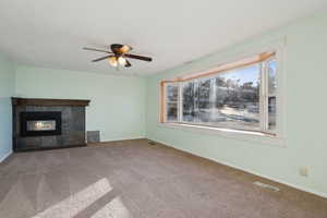 Unfurnished living room featuring a tile fireplace, a wealth of natural light, carpet, and ceiling fan