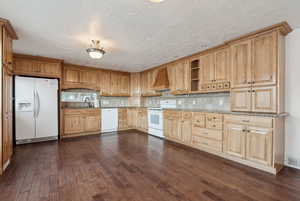 Kitchen featuring light stone countertops, premium range hood, tasteful backsplash, white appliances, and dark hardwood / wood-style floors