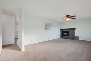 Unfurnished living room featuring carpet flooring, ceiling fan, and a fireplace