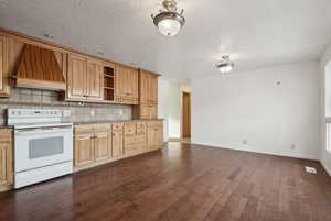 Kitchen featuring backsplash, premium range hood, dark wood-type flooring, light brown cabinets, and white electric range