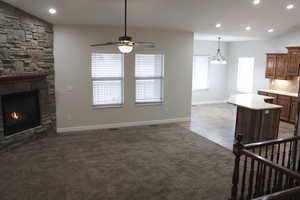 Great room with a fireplace, light tile patterned floors, ceiling fan with notable chandelier, and lofted ceiling