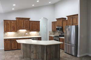 Kitchen featuring high vaulted ceiling, sink, tasteful backsplash, a kitchen island, and stainless steel appliances