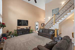 Living room with carpet flooring, ceiling fan, and a towering ceiling