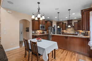 Kitchen featuring backsplash, hanging light fixtures, stainless steel appliances, and custom range hood