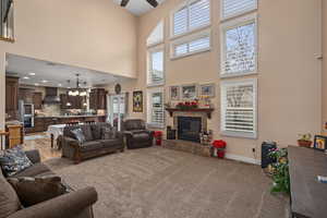 Carpeted living room featuring ceiling fan with notable chandelier, a high ceiling, and a tiled fireplace