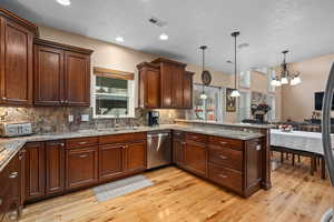 Kitchen with dishwasher, sink, tasteful backsplash, decorative light fixtures, and light wood-type flooring