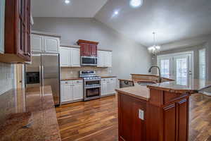 Kitchen with backsplash, stainless steel appliances, sink, decorative light fixtures, and an island with sink