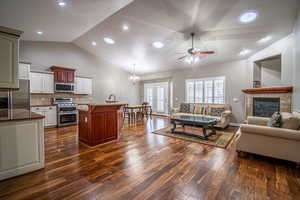 Kitchen with backsplash, white cabinets, vaulted ceiling, a fireplace, and appliances with stainless steel finishes