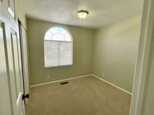 Empty room with light carpet and a textured ceiling