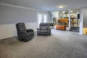 Living area featuring carpet flooring, ceiling fan, crown molding, and french doors