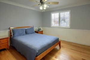 Bedroom with light hardwood / wood-style floors, ceiling fan, and ornamental molding