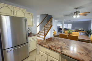 Kitchen featuring stainless steel refrigerator, ceiling fan, light tile patterned floors, and cream cabinetry