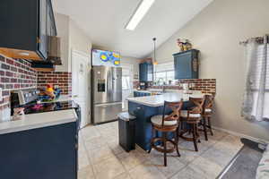 Kitchen with hanging light fixtures, vaulted ceiling, blue cabinetry, kitchen peninsula, and stainless steel appliances