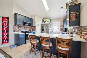 Kitchen featuring pendant lighting, vaulted ceiling, a kitchen bar, kitchen peninsula, and stainless steel appliances