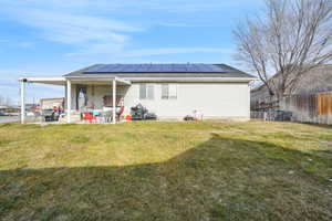 Rear view of house with a lawn, a patio area, and solar panels