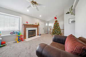 Living room with a tile fireplace, light carpet, vaulted ceiling, and ceiling fan