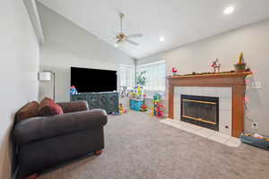 Living room featuring a fireplace, light colored carpet, ceiling fan, and lofted ceiling
