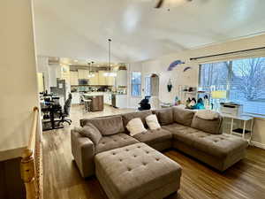 Living room featuring lofted ceiling, a wealth of natural light, ceiling fan with notable chandelier, and light wood-type flooring