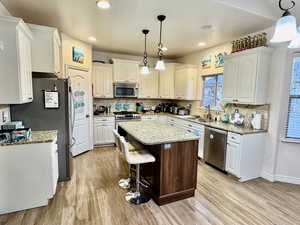 Kitchen with white cabinetry, stainless steel appliances, and hanging light fixtures