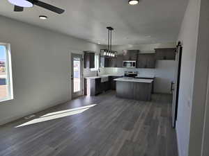 Kitchen featuring dark hardwood / wood-style flooring, stainless steel appliances, a barn door, decorative light fixtures, and a center island