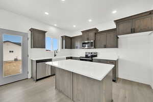 Kitchen with sink, stainless steel appliances, light hardwood / wood-style floors, and a kitchen island