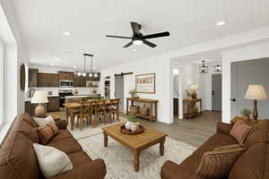 Living room with a barn door, light wood finished floors, ceiling fan, recessed lighting, and baseboards