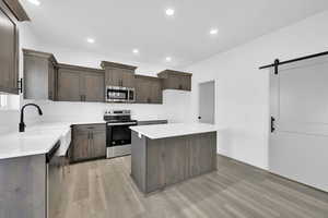 Kitchen featuring a kitchen island, appliances with stainless steel finishes, a barn door, and light hardwood / wood-style flooring